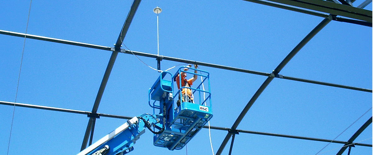 Installer mounting a Preventor ESE air terminal from a boom lift during commercial construction